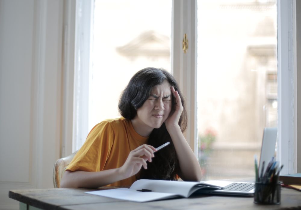 Young girl in yellow shirt at a desk with a notebook looking stressed